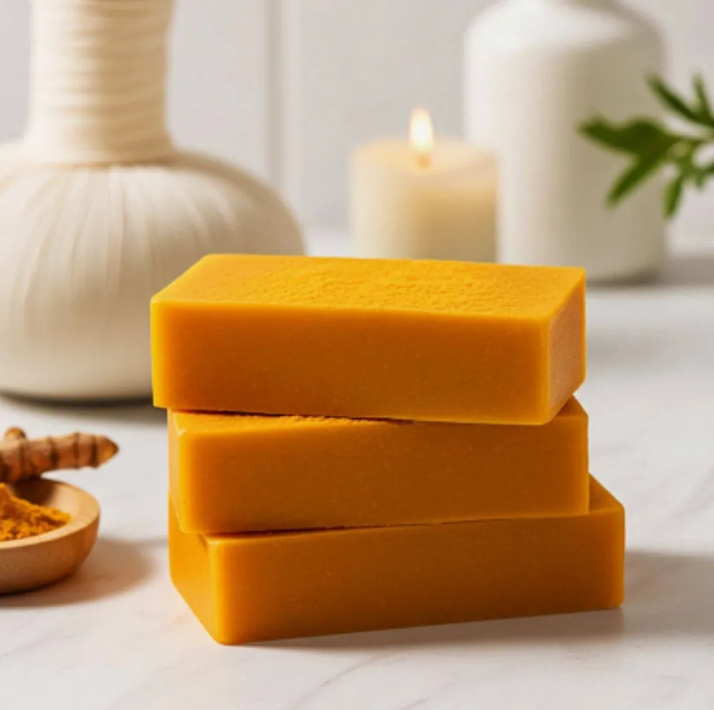 Trois savons au curcuma Open Shop empilés sur un plan de marbre, à côté d'un bol de curcuma en poudre.